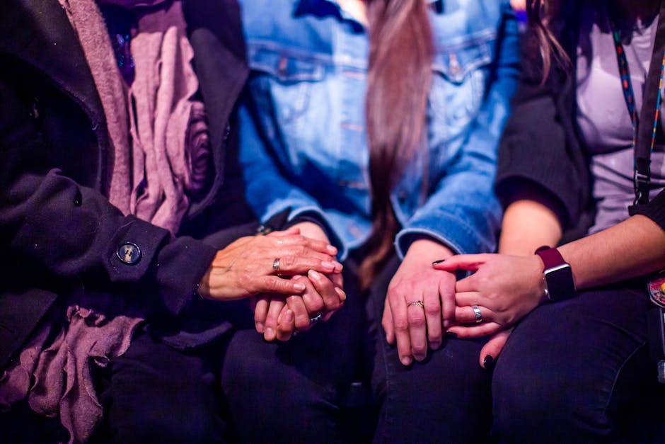 Three women holding hands, symbolizing support and empathy in a warm setting.