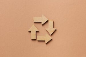 Close-up of a recycling symbol made from wooden arrows on a beige background.