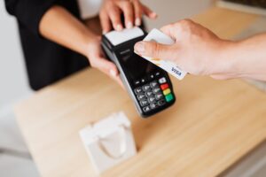 Close-up of hands using a contactless payment terminal with a credit card indoors.