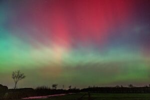 Vibrant Northern Lights in colorful hues fill the night sky above serene landscape.