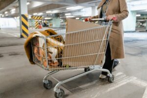 A person pushes a shopping cart with boxes and blankets in a parking garage.