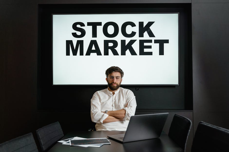 Businessman in modern office setting with a stock market display, looking thoughtful and analytical.