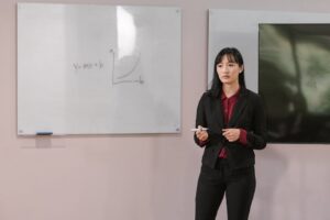 Businesswoman presenting on a whiteboard explaining financial concepts indoors.