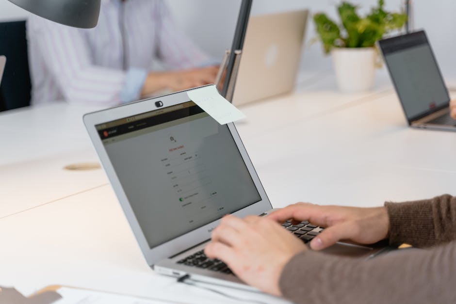 Close-up of a professional working on a laptop with a sticky note in a modern office setting.