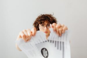 A determined woman in eyeglasses tearing a paper indoors.